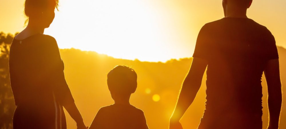 Mutter, Vater und Kind fassen sich an den Händen und sehen in den Sonnenuntergang. Symbol für Familienfreundlichkeit und Begleitbild für die Umfrage zur Familienfreundlichkeit, die noch bis 31.12.2024 in der Stadt Hamm durchgeführt wird.