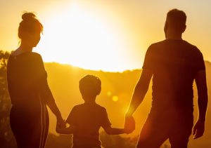 Mutter, Vater und Kind fassen sich an den Händen und sehen in den Sonnenuntergang. Symbol für Familienfreundlichkeit und Begleitbild für die Umfrage zur Familienfreundlichkeit, die noch bis 31.12.2024 in der Stadt Hamm durchgeführt wird.