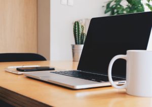 Schreibtisch mit Laptop, Kaffeetasse, Pflanzen. Vom Büro aus kann man ganz flexibel an einem der Online-Termine zur Bürgerbeteiligung teilnehmen