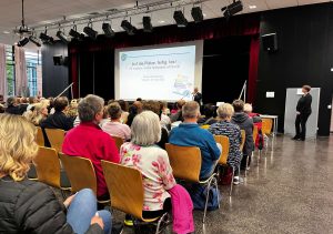 Teilnehmerinnen und Teilnehmer der Auftaktveranstaltung der Bürgerbeteiligung zum Spielplatz-Angebot in Usingen sitzen in Stuhlreihen und hören sich die Ideen und Vorschläge der Stadtverwaltung an.