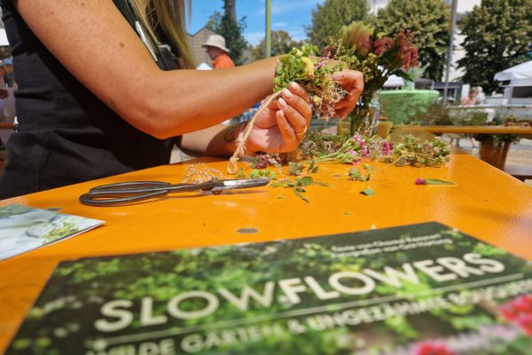 Tisch mit Blumen; Person beim Binden eines Blumenkranzes im Rahmen vom Aktionstag "Mit(te) gemacht" in der Stadt Griesheim.