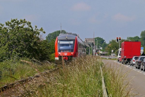 Regionalzug in Richtung Kiel fährt neben einer Straße mit einer Autoschlange. Symbolbild für den landesweiten Nahverkehrsplan Schleswig-Holstein, zu dem im September 2025 Online-Foren mit den relevanten Stakeholdern stattgefunden haben.